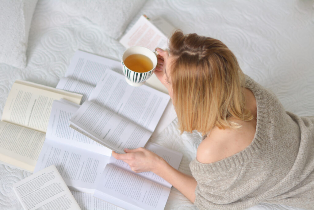 kobieta, włosy do ramion, leży na łóżku, czyta książki.