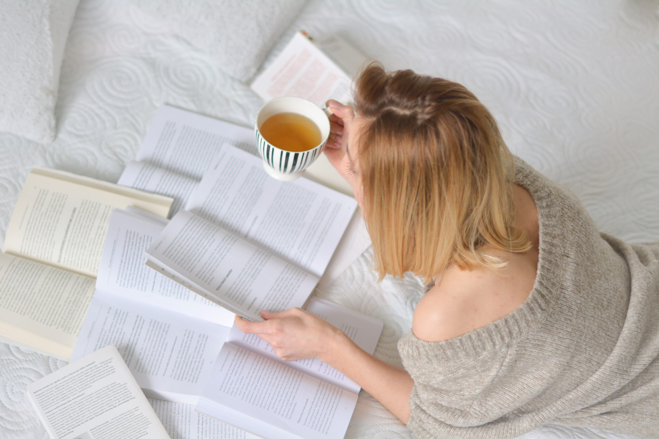 kobieta, włosy do ramion, leży na łóżku, czyta książki.