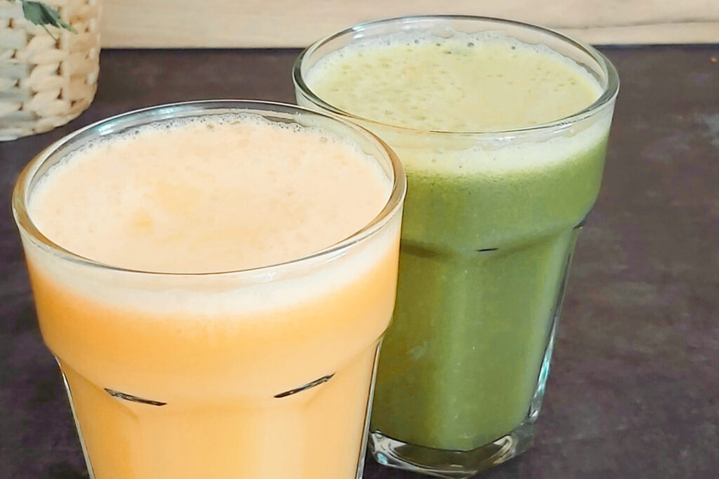 Dwie szklanki wypełnione sokiem. W jednej sok koloru zielonego. W drugiej sok koloru pomarańczowego. 